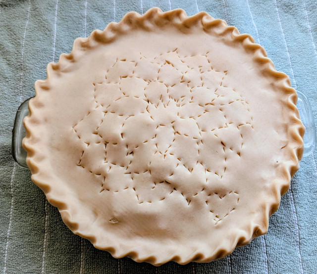 Pie waiting to go into the oven. There is a dahlia design in the crust. 
