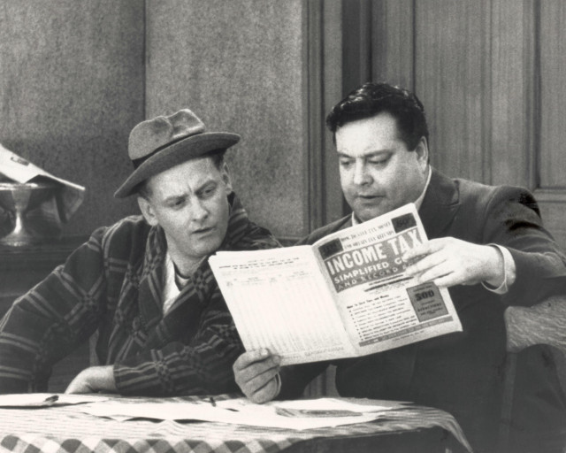 Ed (in his robe) "helps" Ralph (in his bus uniform) try to figure out where he went wrong on his tax return. 