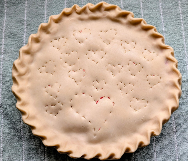 An uncooked berry pie sitting on a blue kitchen towel. The vent pattern is hearts.