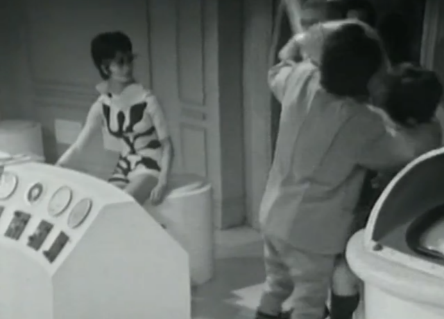 A women sits at a computer desk. Her costume is a unique pattern of lines that is an abstract version of a circuit board.