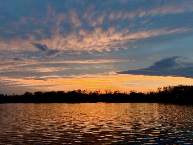 Photograph of a sunset over a lake with orange clouds reflected in the ripples in the water.