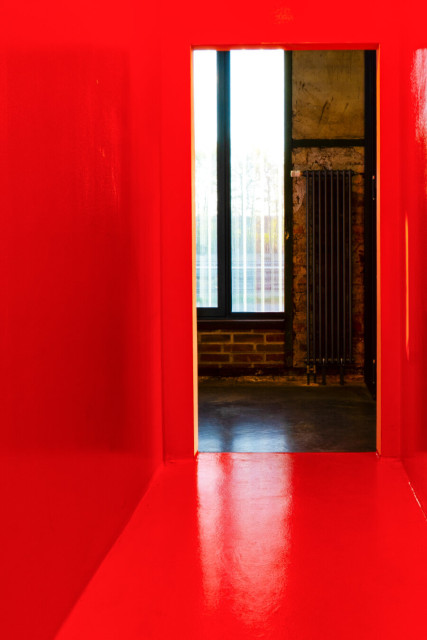 Blick aus einem orangefarbenen Raum durch einen Türauschnitt auf ein Fenster und eine Heizung. Die Tür fehlt.