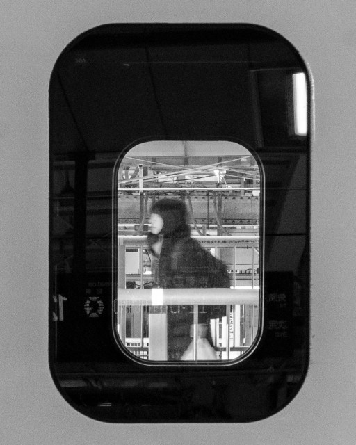 Black and white photo of a figure seen through a Shinkansen window at a Tokyo train platform for #FensterFreitag. 