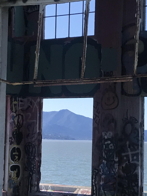 San Francisco Bay and Mount Tamalpais are shown in a window frame in the ruins of a warehouse building. It's a sunny day. Above the opening is a smaller window opening with the panel borders still intact. Photo taken at Miller/Knox Regional Shoreline park in Point Richmond, CA.