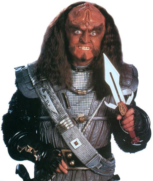 Gowron, Chancellor of the Klingon High Council, from the TV show Star Trek the next generation, holding a large dagger and smiling