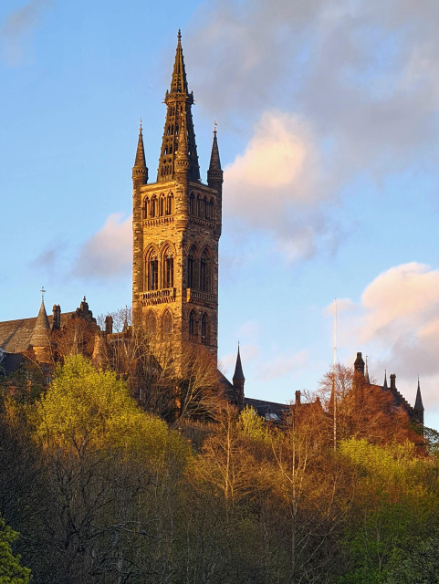 The gothic tower of Glasgow University rising above trees which are just coming into leaf.