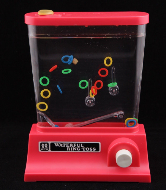 A red Waterful Ring-Toss toy by Tomy, a box filled with water where you try to land small plastic ring into various pegs by pushing a button that propels the ring upwards when pushed.