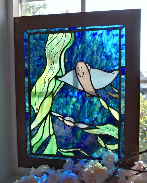 Framed stained glass of a bat ray and kelp piece against a window.