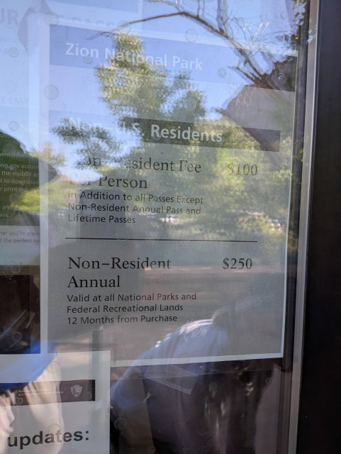 Difficult to read sign posted behind glass that informs non-US residents they must cough up an additional fee of $100 to enter Zion NP in Utah.
