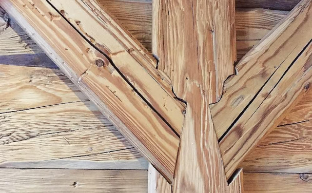[epo] Proksimfoto de la ligna kunigaĵo inter fosto kaj du apogiloj. 

[eng] A close up of the timber joinery between a podt and two braces.