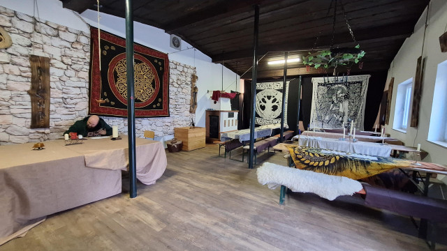A wide room, decorated with sheets, wall carpets, one man sitting off to the side