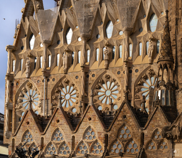 Color photo of the eastern side of the Sagrada Família basilica in Barcelona with rows of windows of different shapes and sizes reflecting the early morning light.