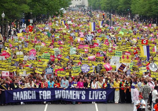 The mall in DC filled with people holding placards for equality. the front row of the march is holding a large banner reading "march for women's lives".
