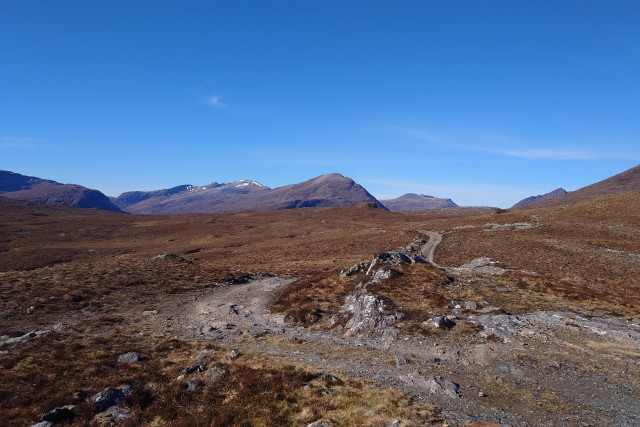A rocky track curves away across a rocky heather landscape to distant mountains