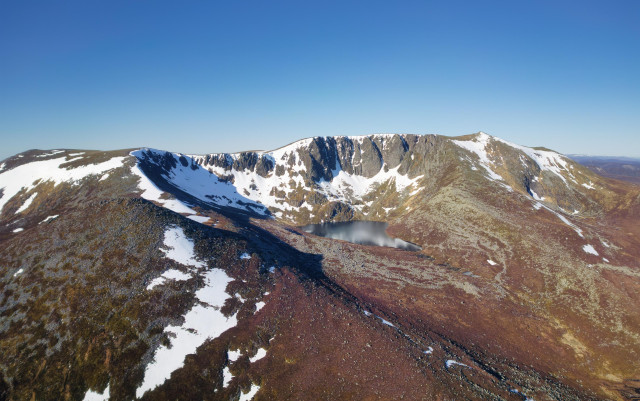 An aerial view of a mountain with some snow cover under a blue sky. Lochnagar. Cairngorms NP, Scotland
