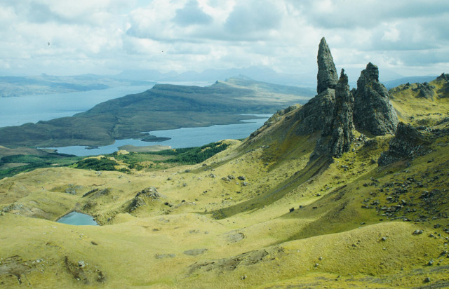 View over the ragged grassy landscape of Skye with three rocky peaks in the foreground and the sea behind