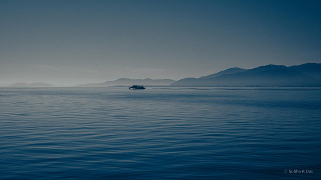 Very blue picture taken from a boat/ferry of the blue waters of Lake Biwa with blue slight hazy sky and dark silhouette of mountains mostly to the right breaking up the horison and in the distance almost center of frame a boat/ferry in the water
Lake Biwa Nov 2025 #Japan