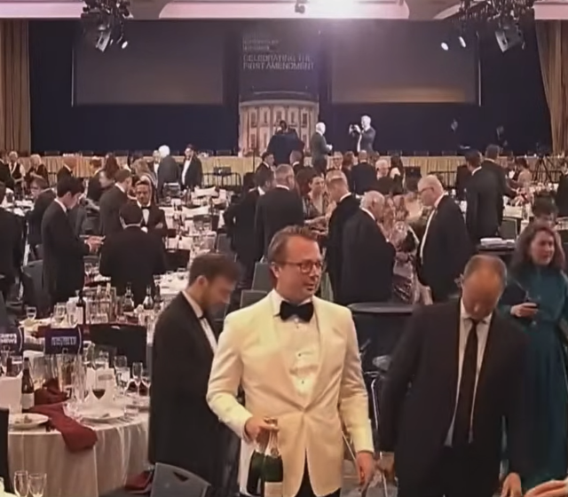 A man in a tuxedo leaving the White House Correspondents' Dinner holding two bottles of what appears to be champagne.