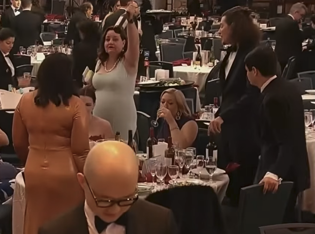A woman holding an unopened bottle of wine above her head at the White House Correspondents' Dinner.