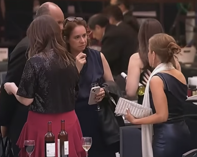 A woman at the White House Correspondents' Dinner walking away from a table with a bottle of wine under her arm.
