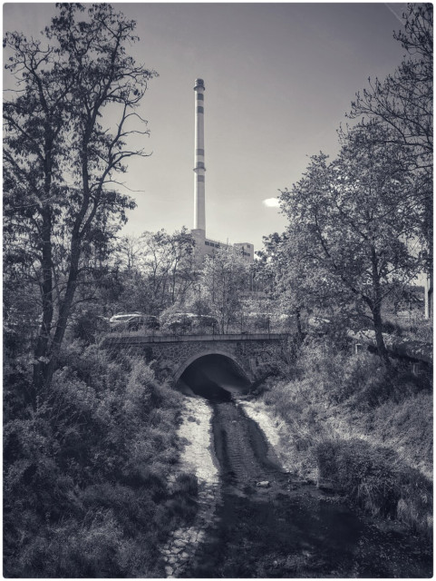 The scene shows a smoke stack and a factory in the upper part of the image and the bottom part of the image is a creek and it looks like the sewage is coming from the actual smoke stack.
