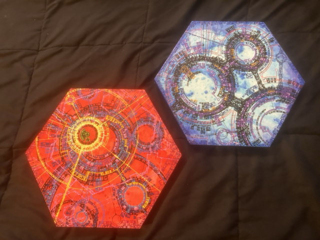 Two hexagonal Complex geometric abstract arts, one mostly red with yellow highlights, the other a set of dark circular frameworks over a blue and white cloud background.