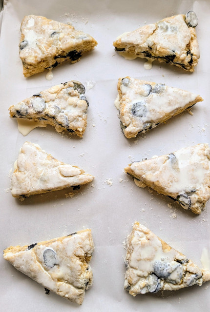Triangular shaped scones are brushed with heavy cream. The parchment paper lined baking sheet will go in the freezer for an hour before baking. 