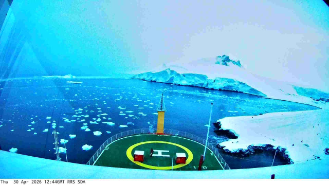 View from a webcam mounted on the RRS Sir David Attenborough boat. Typically you'd see the front of the ship with a helipad, and the sea waters surrounding the ship. Depending on the current location of the ship, the scenery may include icebergs and industrial ports.