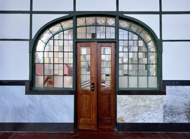 Petite porte en bois ancienne insérée dans une partie vitrée décorative en demi-lune, composée de carreaux dépolis et pour certains colorés.
