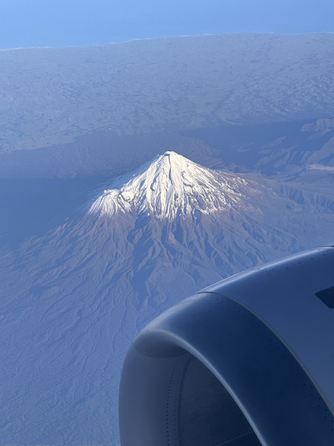 Photo of a snow covered volcano from the window of an aeroplane - you can see one of the engines. 