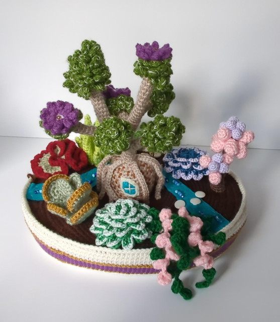The back view of the planter. The back of the broccoli tree has an irregularly-shaped felt window. The small plants on this side include a gold and pale green thing with round leaves, a medium green rosette with white-frosted leaf edges, and a dangling plant with pink and dark green strands.