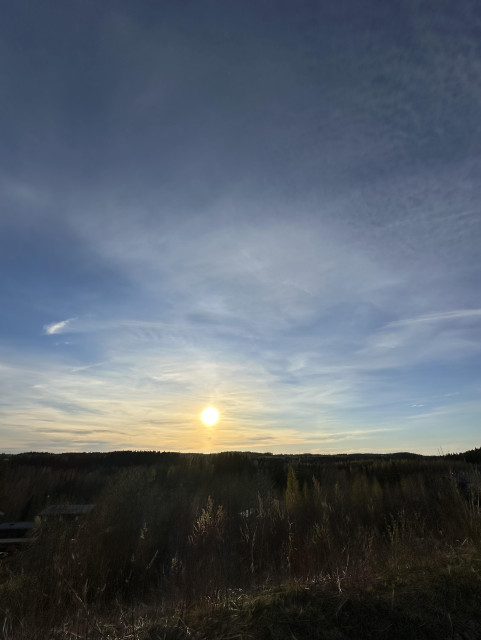A sunset over a forested landscape with a partly cloudy sky.