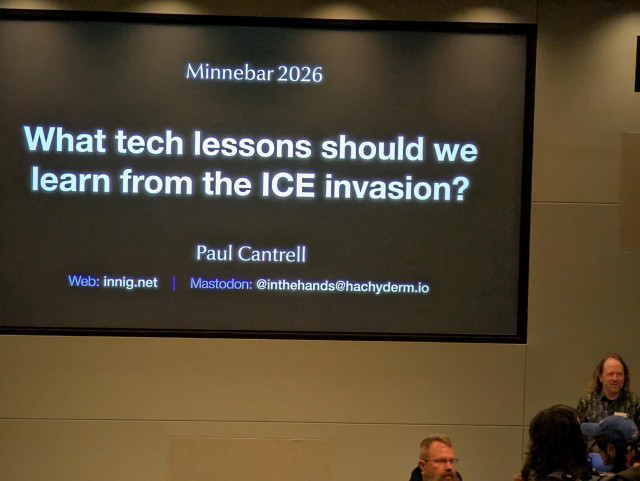 A speaker stands to the right of a large screen. On the screen is a title slide which reads, "What tech lessons should we learn from the ICE invasion?"