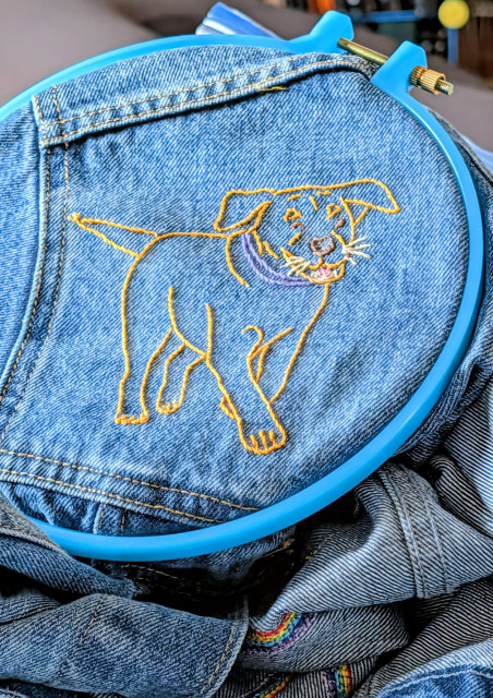 Attempt at embroidered likeness of a golden lab sewn on the front shoulder of a denim jacket. 