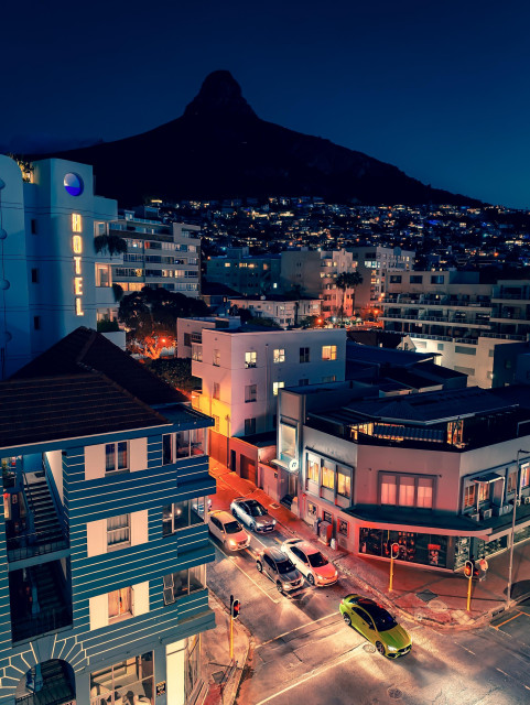 An evening view from a hotel room in Sea Point, Cape Town. The silhouette of Lion's Head looms over the city, cars queuing below in the streets.