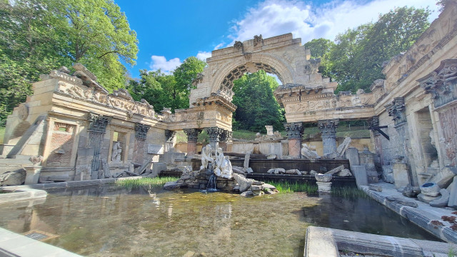 A fake romen ruin atop a fountain under blue skies