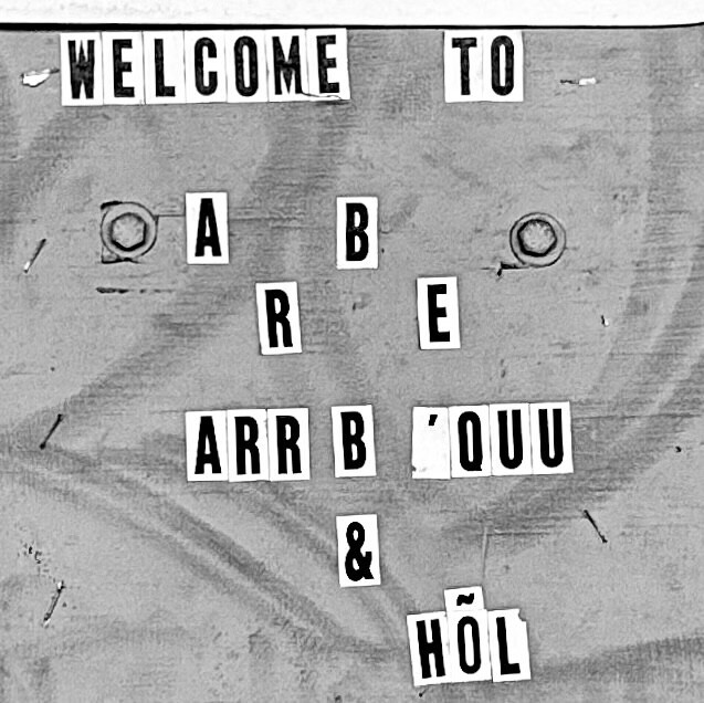 Black and white photo of the entrance to a bar which has a series of stick-on letters spelling out what seems to be nonsense or maybe I just need to learn how to crack the code. Welcome to A B R E ARR B 'OUU &amp; HÕL