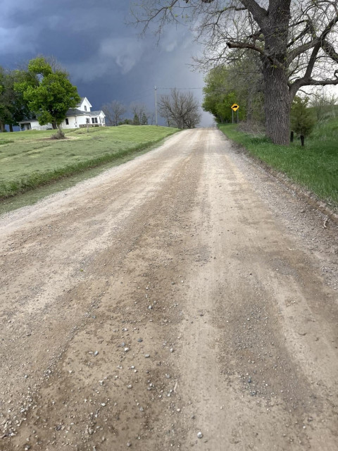 A nice sunny bike ride on a dirt road when I entered the woods suddenly has a giant hail and lightning storm looming. A lone white country house is on the left with dark roiling clouds behind. Right over the hill is where my son met me a minute later to load up the bike as the hail started.