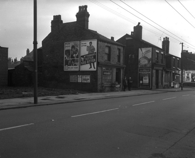 b/w street photo including film poster for: Help / Mozambique / Darby O'Gill and the Little People / The Toast of New Orleans 