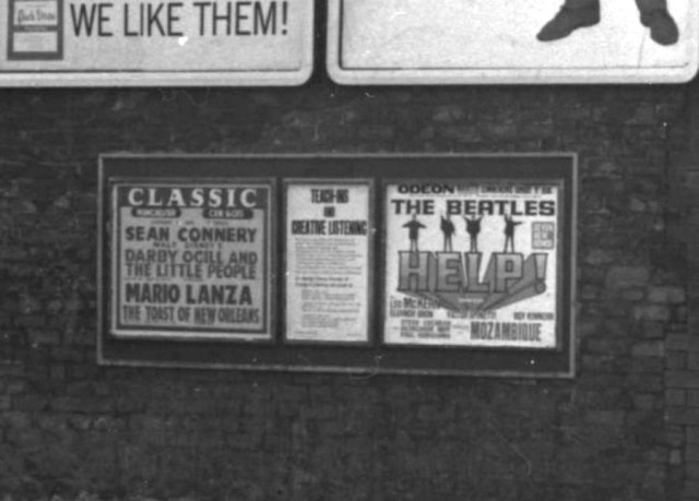 b/w street photo including film poster for: Help / Mozambique / Darby O'Gill and the Little People / The Toast of New Orleans  (close up)
