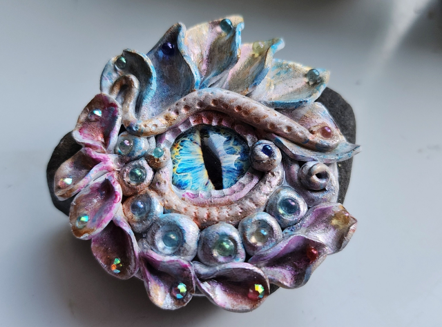 A dragon eye with a blue and gold iris, and white scales with pastel blue, pink, and gold hues