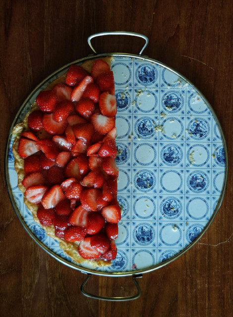 A photo of half of a round cake with fresh strawberries, on a blue and white round plate.