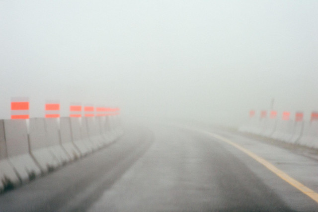 We are driving through a construction zone.  Concrete walls have been placed to keep us in one lane.  At the tops of the concrete blocks are bright orange markers.  It is really foggy, so it looks like we are about to driven into nowhere. 