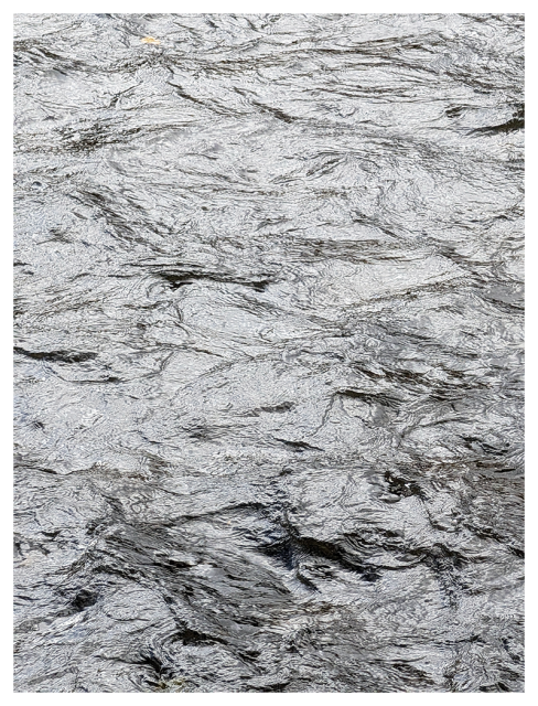 	close-up view of rippling water, showing textured, wavy patterns on the surface. the water reflects light, creating shimmering and metallic gray tones with hints of movement and depth throughout. 

