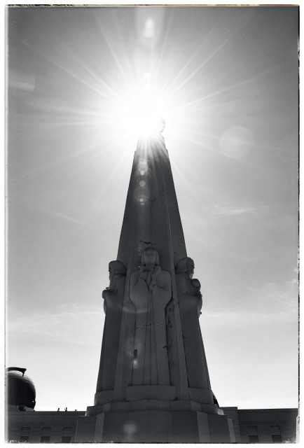 The sun at noon, shining brightly at the top of the Astronomers Monument at Griffith Park in Los Angeles. 

The monument is a carved obelisk with scientific figurines standing in front of the Griffith Observatory. And the sun is the sun.

Monochrome... with great lens flare: a starburst and lots of little circular globes radiating outward from the sun. I love lens flare.