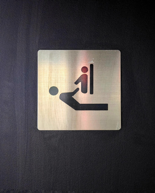 A tilted photo of a metallic sign with two figures, indicating a place to 'change' babies.