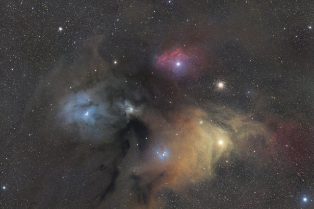 A field of stars with a large region of gas and dust. There are a number of vividly colored areas.