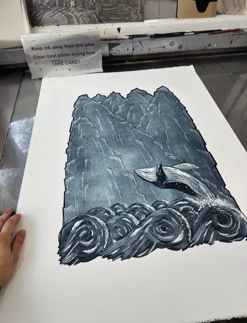 Full print shown at an angle with a hand for scale, the print is A2 on larger paper. The etching plate was laser cut into the outline shape of the waves and mountains. 