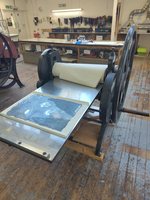 The etching plate sat on an big old cast iron Rochat printing press, in a print room with a gnarly old wood floor, big work benches, hotplates and lots of drying scrim in the background 