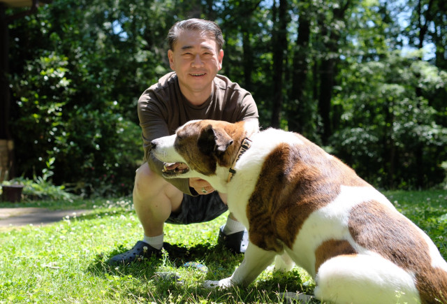 A man and a white and brown dog sitting in the yard on a very sunny afternoon
